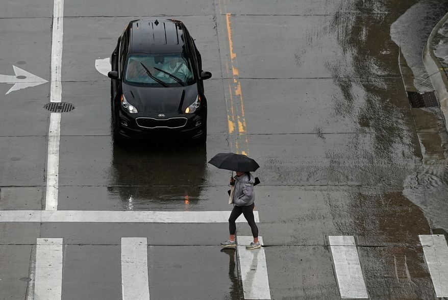 FILE - A pedestrian crosses the street in front of a car on a rainy day in Denver. (AP Photo/David Zalubowski, File)