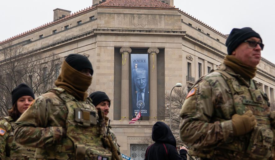 Members of the National Guard walk past a banner with President Donald Trump hanging on the Department of Justice, Thursday, Feb. 19, 2026, in Washington. (AP Photo/Allison Robbert)