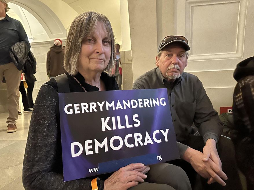 Paula Wood holds a sign protesting Missouri’s congressional redistricting effort while sitting beside her husband, Tim Wood, during a rally on Jan. 21, 2026, at the state Capitol in Jefferson City, Mo. (AP Photo/David A. Lieb)