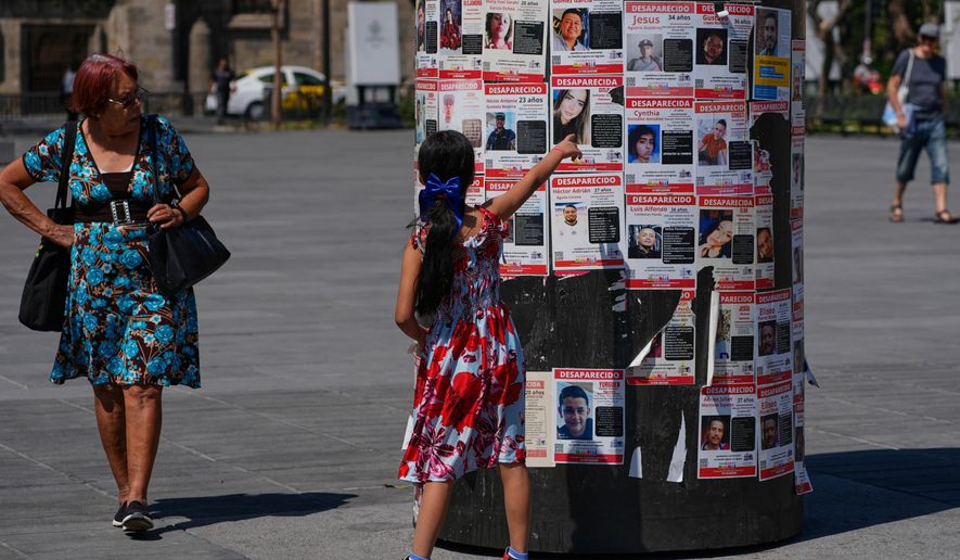 A girl points at posters bearing the faces of missing persons in Guadalajara, Mexico. Wednesday, Feb. 25, 2026. (AP Photo/Marco Ugarte)