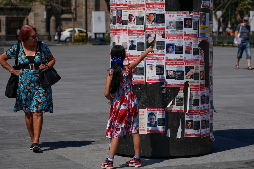 A girl points at posters bearing the faces of missing persons in Guadalajara, Mexico. Wednesday, Feb. 25, 2026. (AP Photo/Marco Ugarte)