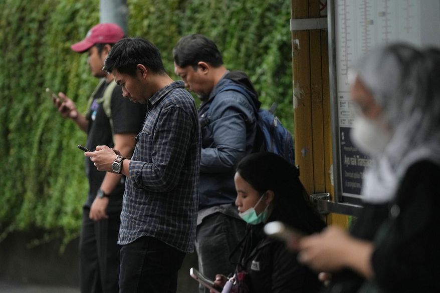 People use their mobile phones at a bus stop in Jakarta, Indonesia, Friday, March 6, 2026. (AP Photo/Dita Alangkara)