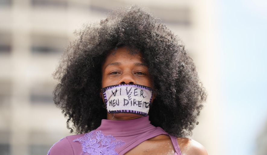 A woman with tape reading in Portuguese "Living is my right" over her mouth takes part in a march marking International Women's Day on Copacabana beach in Rio de Janeiro, Sunday, March 8, 2026. (AP Photo/Silvia Izquierdo)