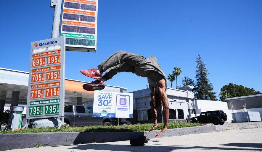 Marcus Hopkins, a street performer, does a backflip in front of advertised gas prices Monday, March 9, 2026, in Los Angeles. (AP Photo/Damian Dovarganes)