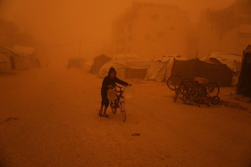 A boy pushes a bicycle carrying jerrycans of water through a sandstorm in Khan Younis, southern Gaza Strip, Saturday, March 14, 2026. (AP Photo/Abdel Kareem Hana)