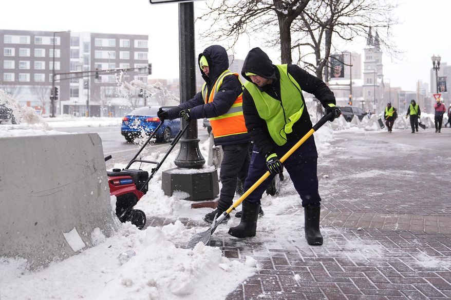 Workers clear snow off the ground Sunday, March 15, 2026, in St. Paul, Minn. (AP Photo/Abbie Parr)