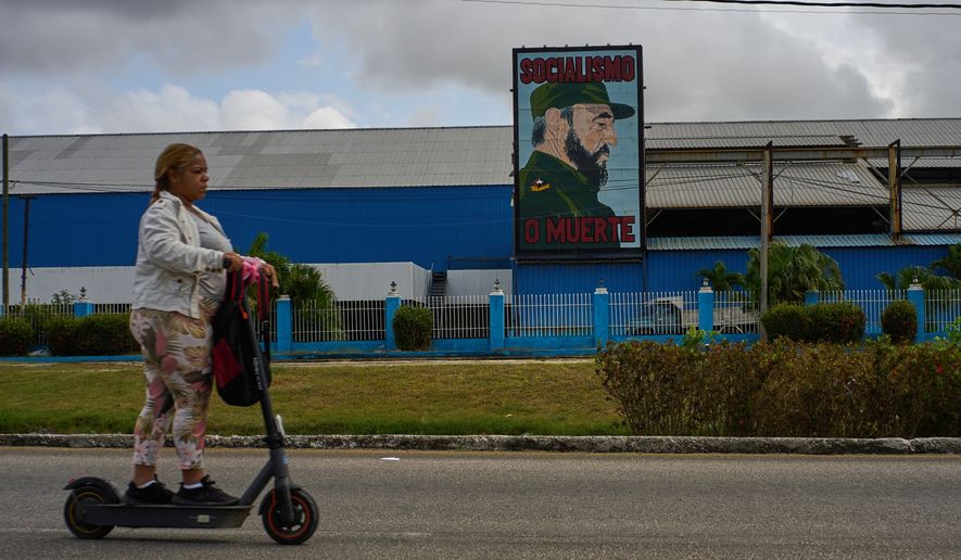 A woman rides an electric scooter past a factory displaying an image depicting the late Cuban leader Fidel Castro, bearing the words "Socialism or Death", in Havana, Cuba, Thursday, March 19, 2026. (AP Photo/Ramon Espinosa)