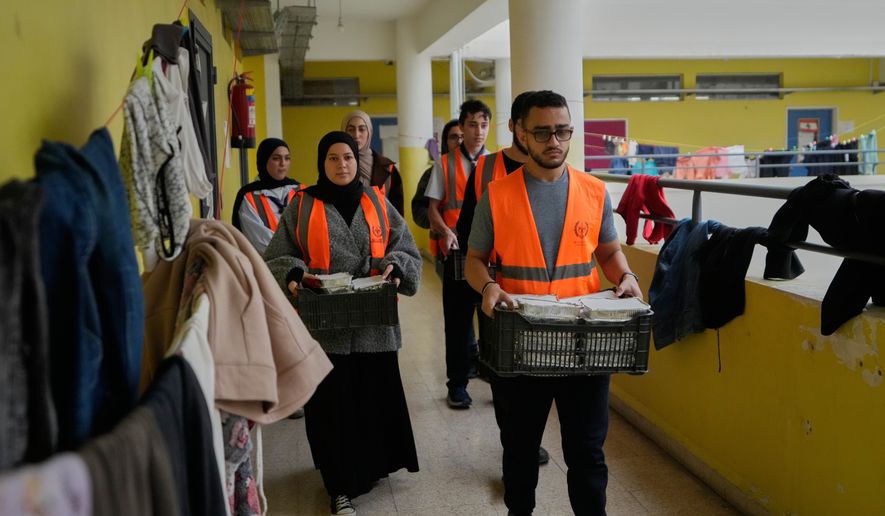 Volunteers carrying meals to be distributed for displaced people who fled Israeli strikes from south Lebanon at a school turned into a shelter, in the southern port city of Sidon, Lebanon, Saturday, March 14, 2026. (AP Photo/Mohammed Zaatari)