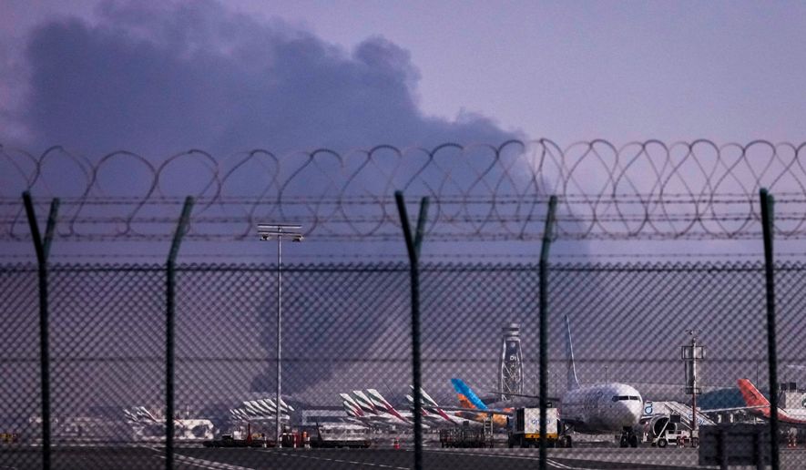Planes are parked at Dubai International Airport as smoke rises in the background after a drone struck a fuel tank early morning, forcing the temporary suspension of flights, in Dubai, United Arab Emirates, Monday, March 16, 2026. (AP Photo)
