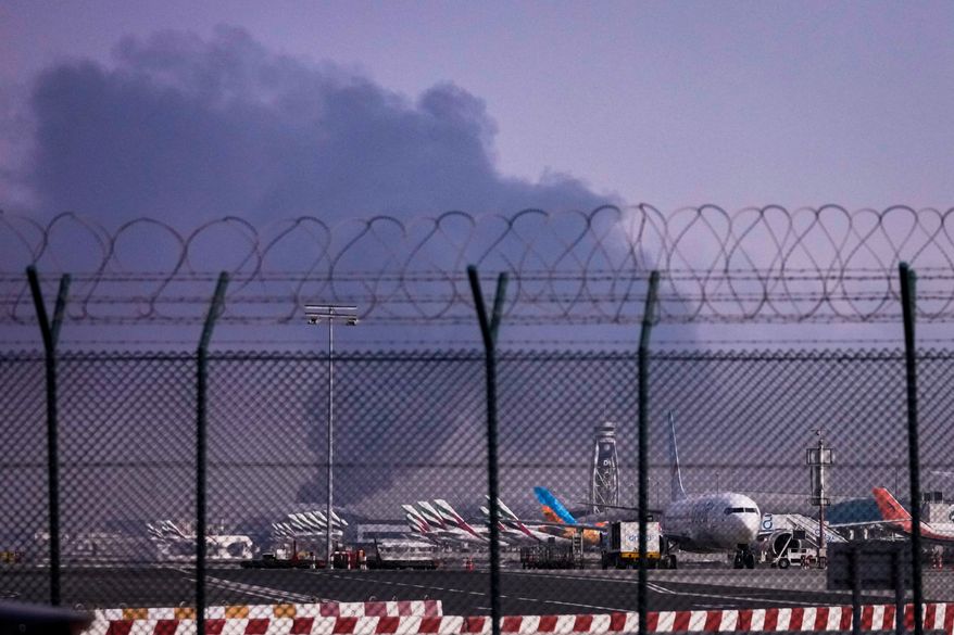 Planes are parked at Dubai International Airport as smoke rises in the background after a drone struck a fuel tank early morning, forcing the temporary suspension of flights, in Dubai, United Arab Emirates, Monday, March 16, 2026. (AP Photo)