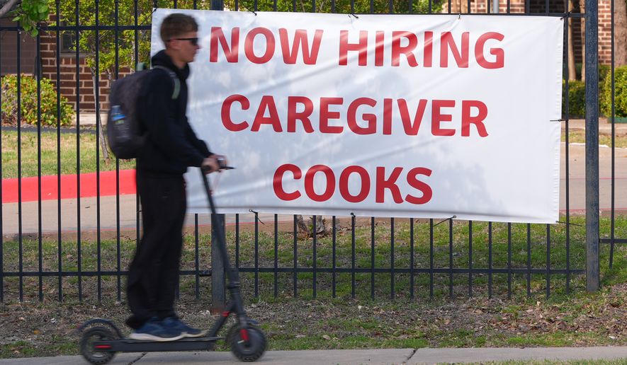 A now hiring sign sits by the sidewalk as a rider on a scooter passes in Garland, Texas, Monday, March 23, 2026. (AP Photo/LM Otero)