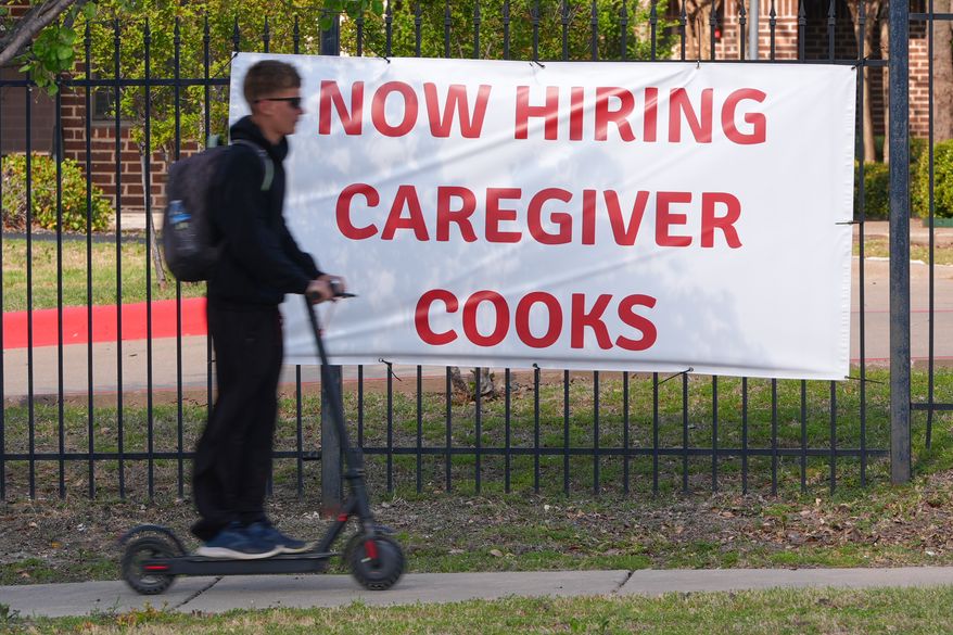 A now hiring sign sits by the sidewalk as a rider on a scooter passes in Garland, Texas, Monday, March 23, 2026. (AP Photo/LM Otero)