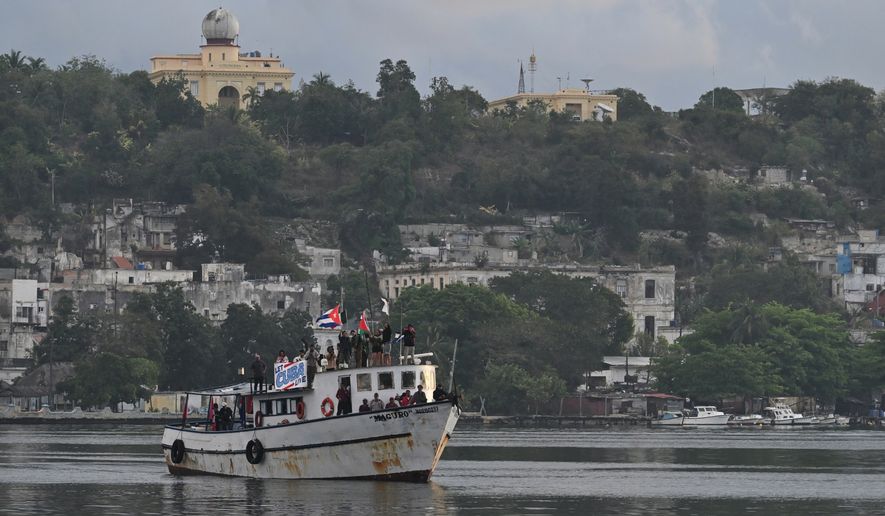 Activists wave Cuban and Palestinian flags from the vessel Maguro, arriving from Mexico with humanitarian aid as part of the "Nuestra America," or Our America convoy, in Havana Bay, Cuba, Tuesday, March 24, 2026. (AP Photo/Jorge Luis Banos)