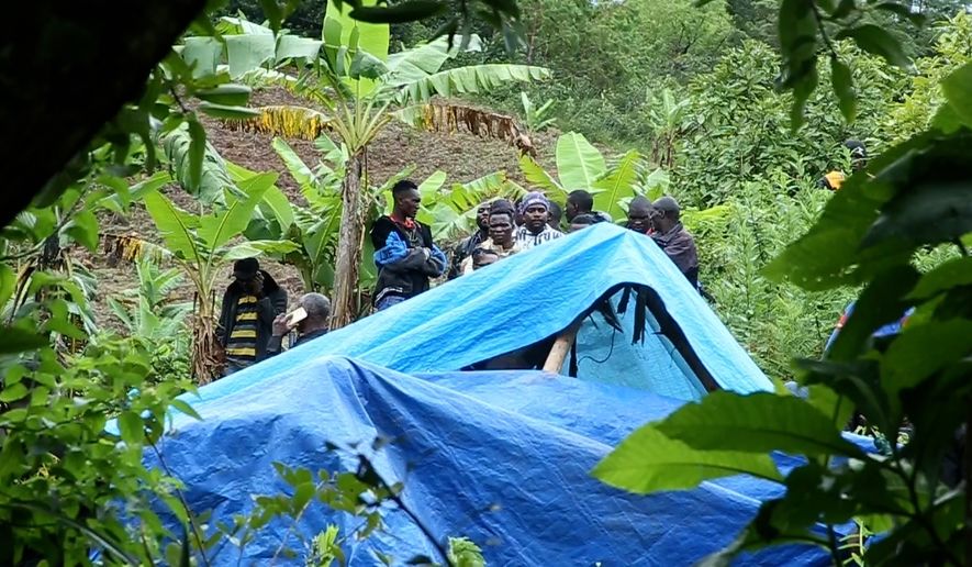 People stand behind a makeshift shelter after heavy rainfalls triggered landslides killing scores Thursday, March 26, 2026 in the Mbeya region of Tanzania Southern Highlands. (AP Photo/Cosmas Muliriye)