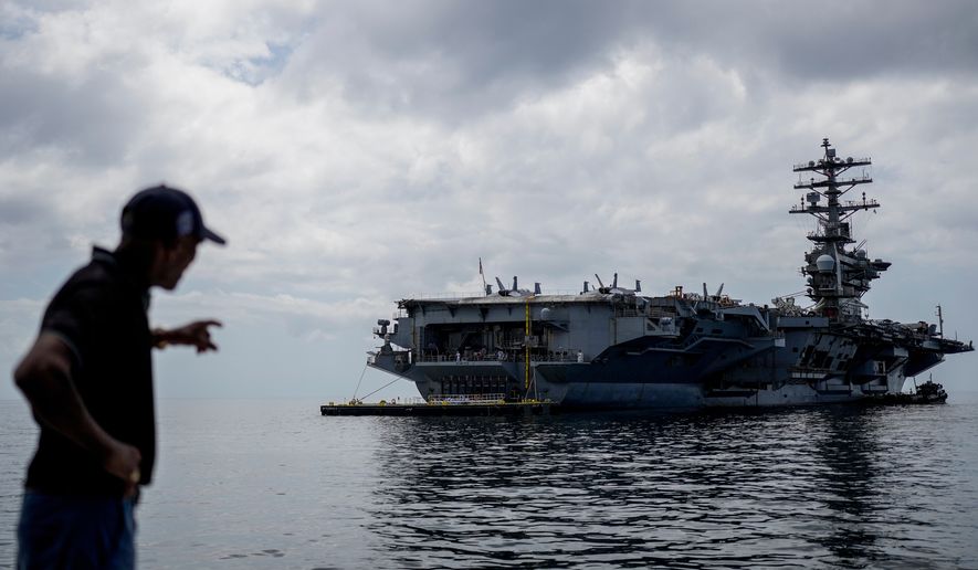 A worker points to the U.S. Navy aircraft carrier USS Nimitz docking in the Gulf of Panama, March 30, 2026. (AP Photo/Matias Delacroix, File)