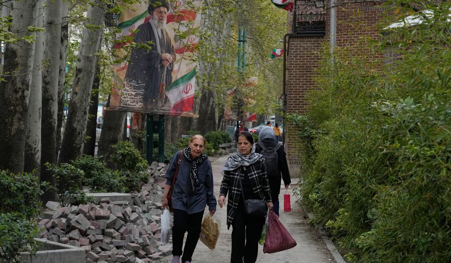 Women walk past a banner depicting the late Iranian Supreme Leader Ayatollah Ali Khamenei, who was killed in the U.S. and Israel strikes on Feb. 28, in northern Tehran, Iran, Sunday, April 12, 2026. (AP Photo/Vahid Salemi)