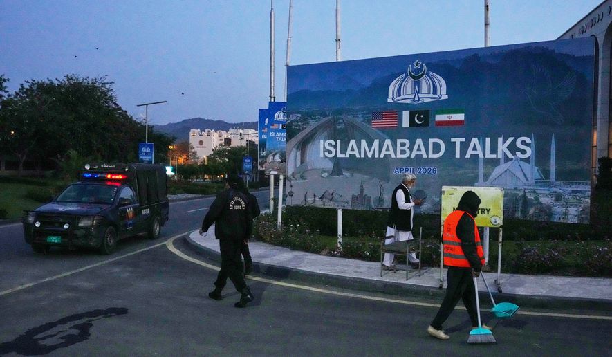 A worker cleans the street as police officers walks towards their vehicle outside a media center close to Serena Hotel, the venue for the U.S. Iran officials meeting, in Islamabad, Pakistan, Sunday, April 12, 2026. (AP Photo/Anjum Naveed)