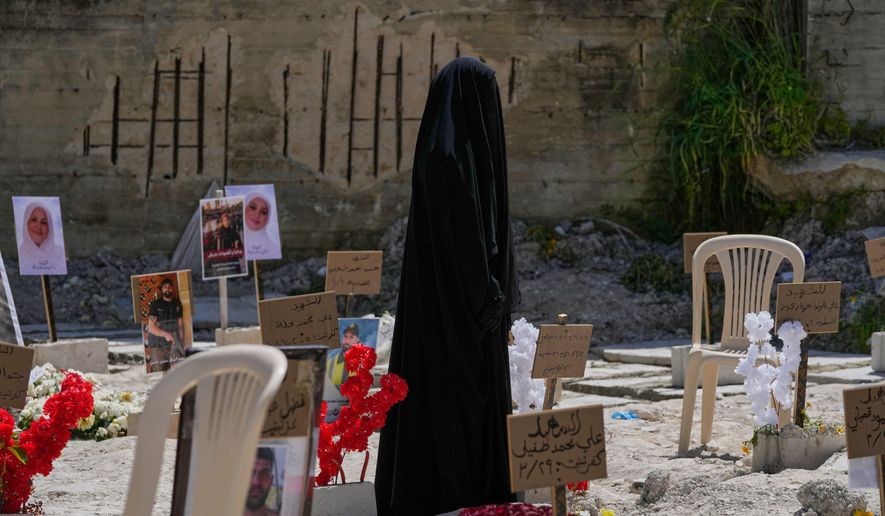 A veiled woman walks through a mass grave where civilians and Hezbollah fighters killed by Israeli airstrikes are temporarily buried in the southern port city of Sidon, Lebanon, Tuesday, April 14, 2026. (AP Photo/Mohammed Zaatari)