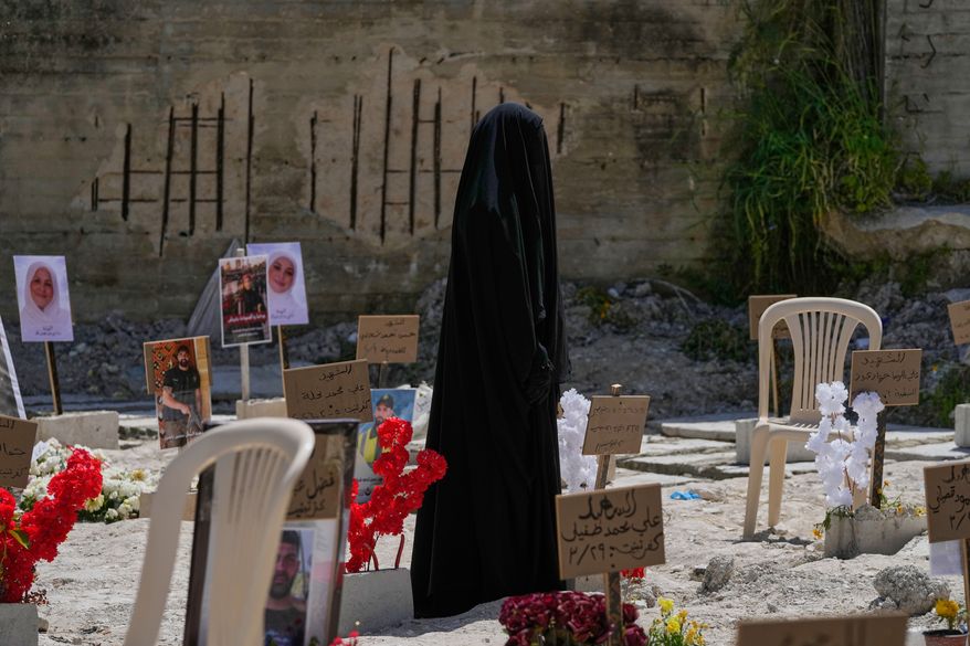 A veiled woman walks through a mass grave where civilians and Hezbollah fighters killed by Israeli airstrikes are temporarily buried in the southern port city of Sidon, Lebanon, Tuesday, April 14, 2026. (AP Photo/Mohammed Zaatari)