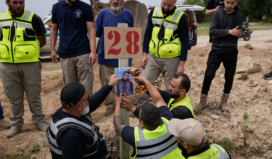 Paramedics attach a portrait over the grave of Ghadir Baalbaki, 19, who was killed on Tuesday in an Israeli airstrike, at a temporary mass grave in the southern port city of Tyre, Lebanon, Wednesday, April 15, 2026. (AP Photo/Hussein Malla)