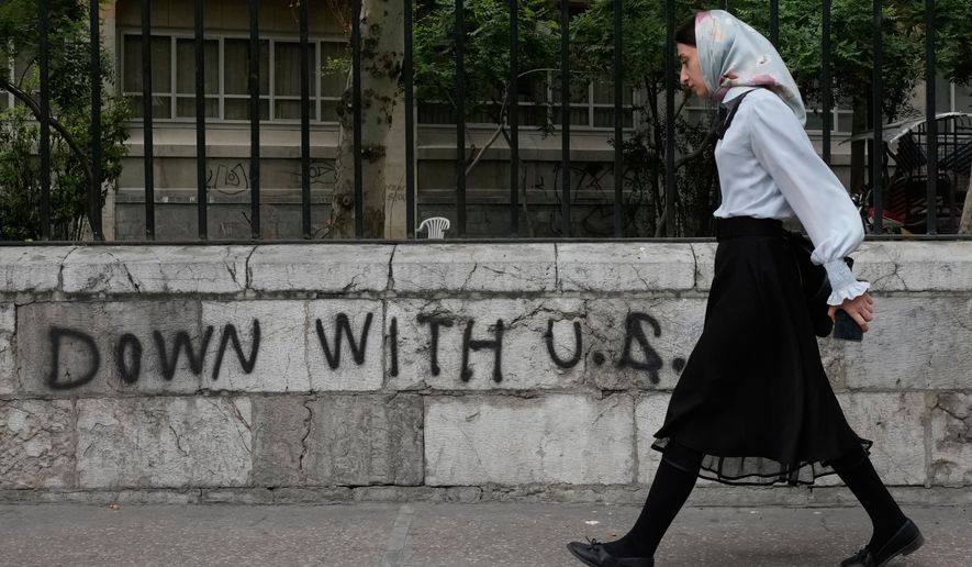 A woman walks past an anti-U.S. graffiti painted on the wall of the Tehran University on Enqelab-e-Eslami (Islamic Revolution) street in downtown Tehran, Iran, Saturday, April 25, 2026. (AP Photo/Vahid Salemi, File)