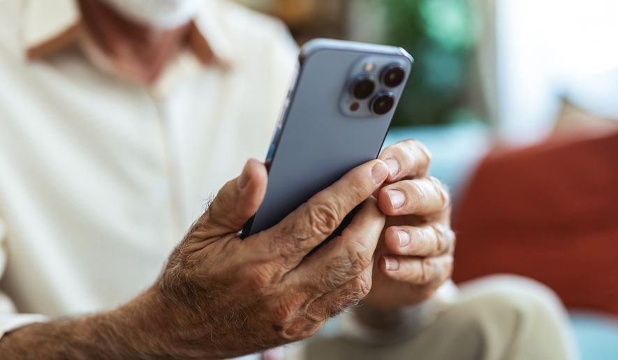 Elderly man uses phone on sofa in home. File photo credit: Jelena Stanojkovic via Shutterstock.