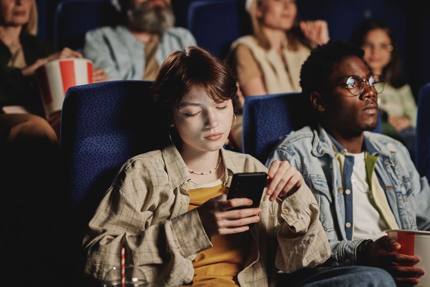 Young woman looks at phone at movie theater. File photo credit: Pressmaster via Shutterstock.