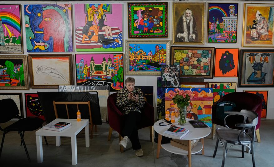 A gallery attendant sits in an armchair near the wall covered with paintings by Ukrainian artists at the Art Kyiv 2026 Festival at the Art Ukraine Gallery in Kyiv, Ukraine, Friday, May 8, 2026. (AP Photo/Efrem Lukatsky)