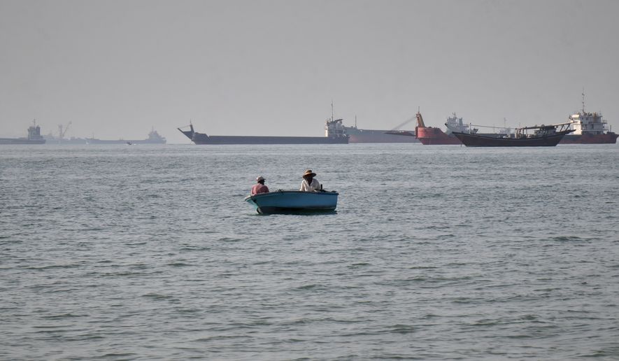 Two men sit in a small boat on the water as a mix of bulk carriers, cargo ships, and service vessels line the horizon in the Strait of Hormuz off Bandar Abbas, Iran, Monday, April 27, 2026.(Razieh Poudat/ISNA via AP)