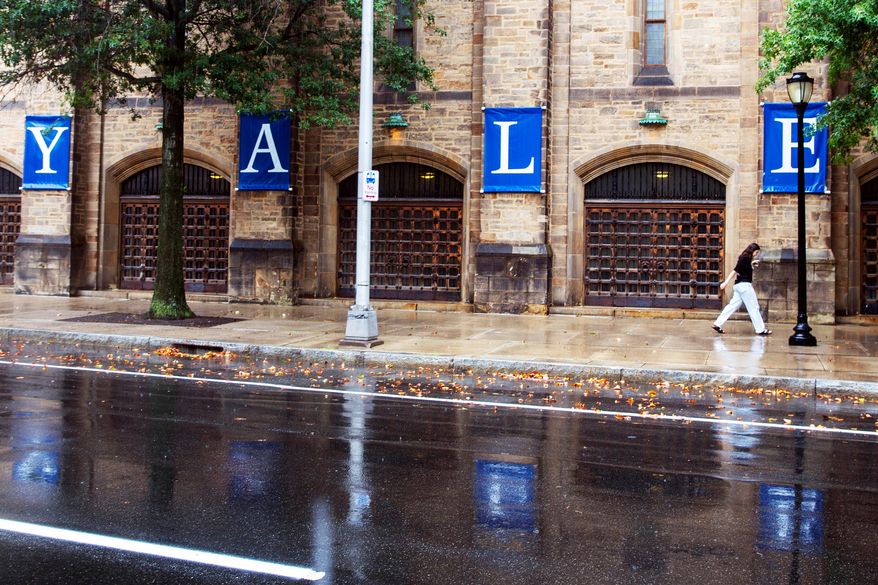 A woman walks by a Yale sign reflected in the rainwater on the Yale University campus in New Haven, Conn., Aug. 22, 2021. (AP Photo/Ted Shaffrey, File)