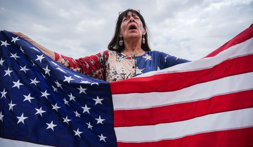 Kathy Fain, from Longview, Texas, holds an American flag while singing the National Anthem during Rededicate 250, a mostly conservative Christian prayer gathering in honor of the United States' 250th anniversary, on the National Mall, Sunday, May 17, 2026, in Washington. (AP Photo/Julia Demaree Nikhinson) ** FILE **