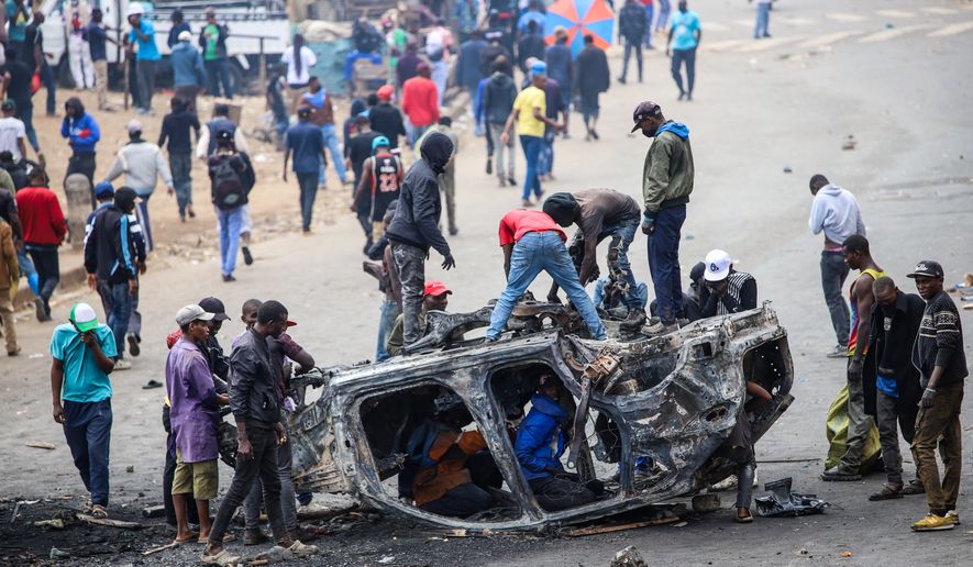 People strip parts from a burned-out vehicle during a public transport strike over fuel prices in Nairobi, Kenya, Monday, May 18, 2026. (AP Photo/Patrick Ngugi)