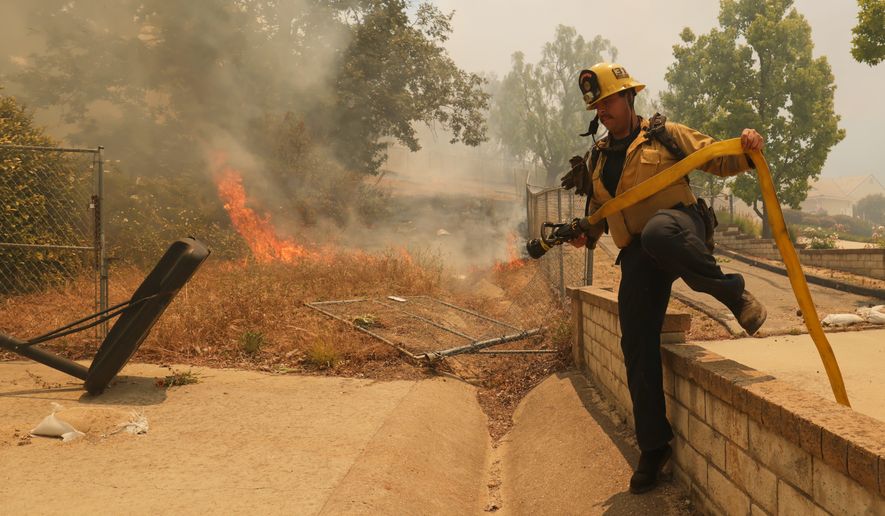 A firefighter hops over a fence while battling the Sandy Fire Monday, May 18, 2026, in Simi Valley, Calif. (AP Photo/Ethan Swope)