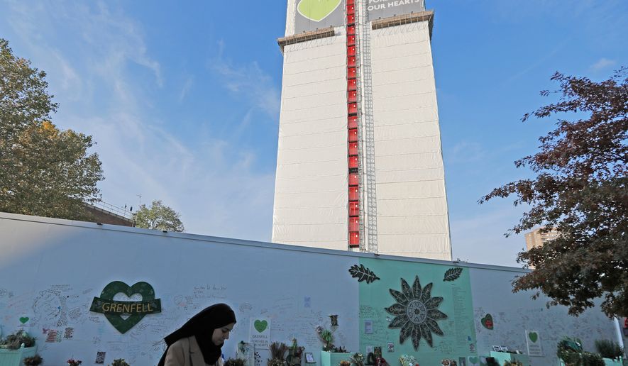 FILE - A woman passes a construction wall with written messages near Grenfell Tower in London, Wednesday, Oct. 30, 2019. (AP Photo/Frank Augstein, file)