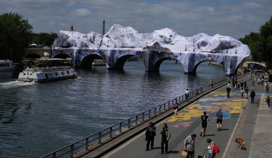 People walk along the Seine river next to "The Pont Neuf Cave," an inflated art installation by French street artist JR, on Paris' oldest bridge, the Pont Neuf, Thursday, May 21, 2026, which will be open to the public from June 6-28. (AP Photo/Michel Euler)