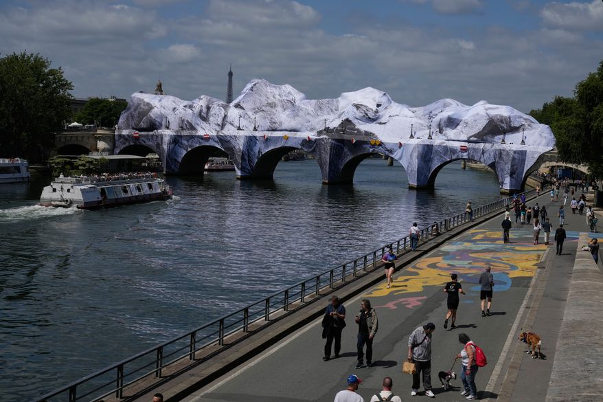 People walk along the Seine river next to "The Pont Neuf Cave," an inflated art installation by French street artist JR, on Paris' oldest bridge, the Pont Neuf, Thursday, May 21, 2026, which will be open to the public from June 6-28. (AP Photo/Michel Euler)