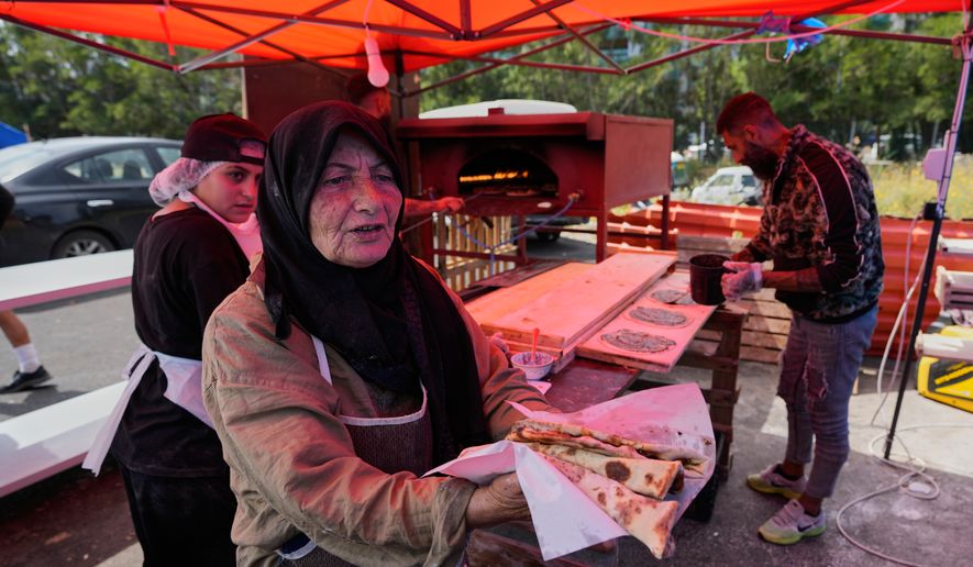 Soubhiye Zeiter, 63, a displaced woman who fled her home with her family in Beirut's southern suburbs due to the war between Israel and Hezbollah, distributes mana'eesh, a popular Lebanese flatbread breakfast topped with thyme at a small bakery in a tented settlement along Beirut's waterfront, Lebanon, Thursday, May 21, 2026. (AP Photo/Hussein Malla)