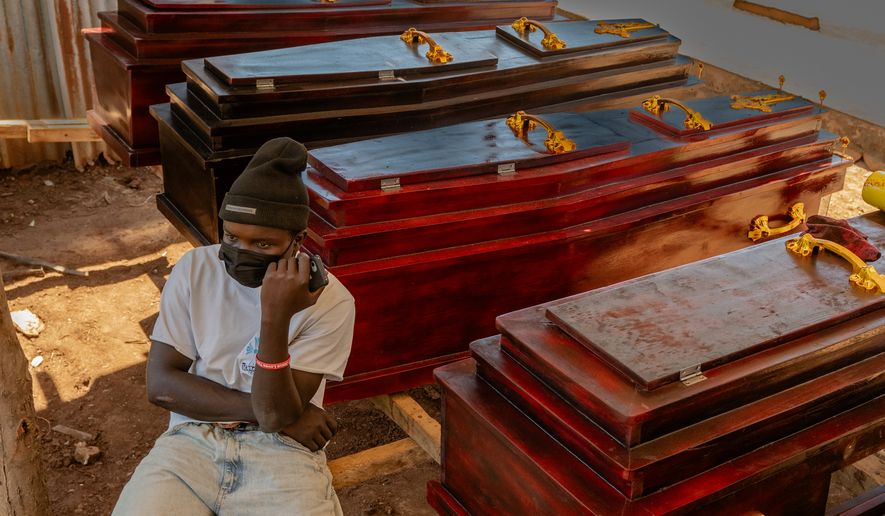Djakisa Christian, 18, a funeral home manager, sits in front of coffins for sale at his shop in Bunia, Congo, Friday, May 22, 2026. (AP Photo/Moses Sawasawa)