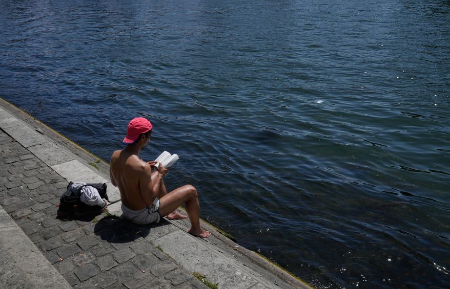 A man reads a book while sitting in the sun along the Seine River in Paris, Monday, May 25, 2026. (AP Photo/Michel Euler)