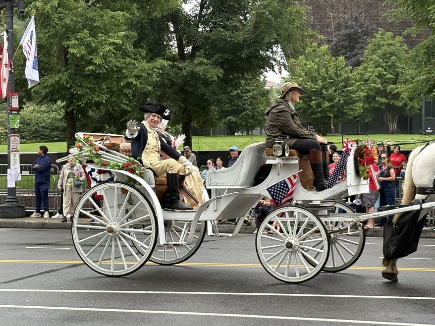 A George Washington impersonator waves to people along Constitution Avenue NW as his carriage rides past the National Museum of African American History and Culture (Matt Delaney/The Washington Times)