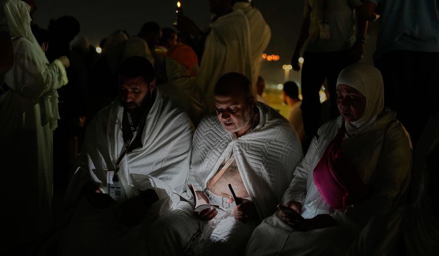 Muslim pilgrims read a copy of Islam's holy book Quran atop of the rocky hill known as the Mountain of Mercy, on the Plain of Arafat, during the annual Hajj pilgrimage near the holy city of Mecca, Saudi Arabia, Tuesday, May 26, 2026. (AP Photo/Altaf Qadri)