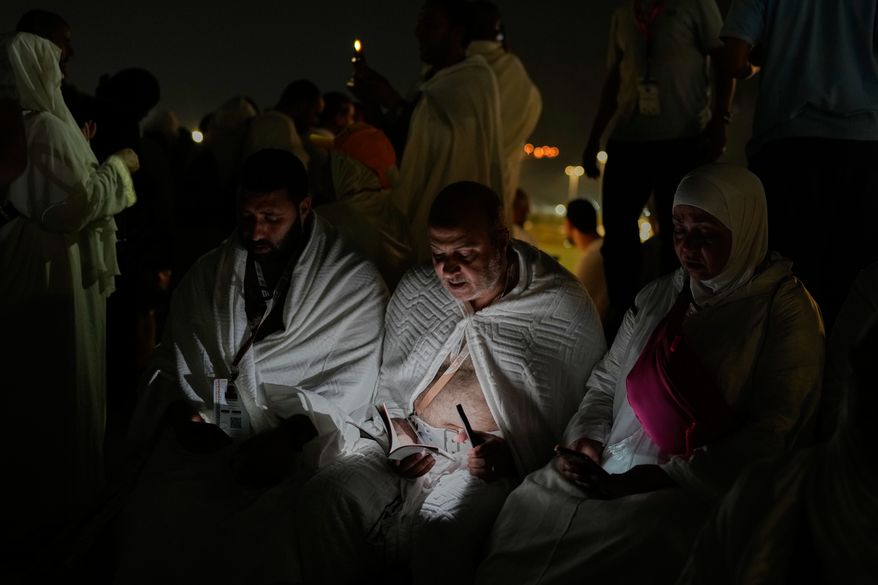 Muslim pilgrims read a copy of Islam's holy book Quran atop of the rocky hill known as the Mountain of Mercy, on the Plain of Arafat, during the annual Hajj pilgrimage near the holy city of Mecca, Saudi Arabia, Tuesday, May 26, 2026. (AP Photo/Altaf Qadri)
