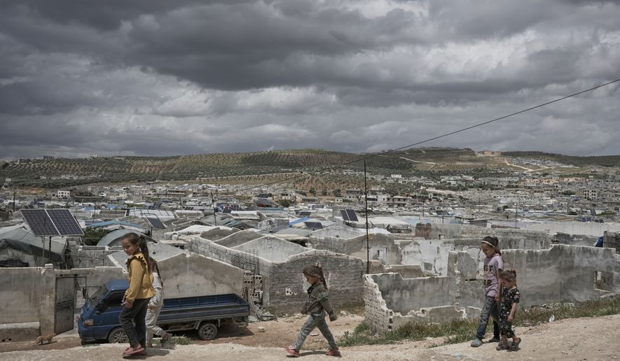 Syrian children walk along a dirt path at the edge of al-Karama camp, built from scratch with light-brick structures covered with fabric and housing internally displaced Syrians near the village of Atmeh, Idlib province, Syria, Tuesday, May 19, 2026. (AP Photo/Omar Albam)