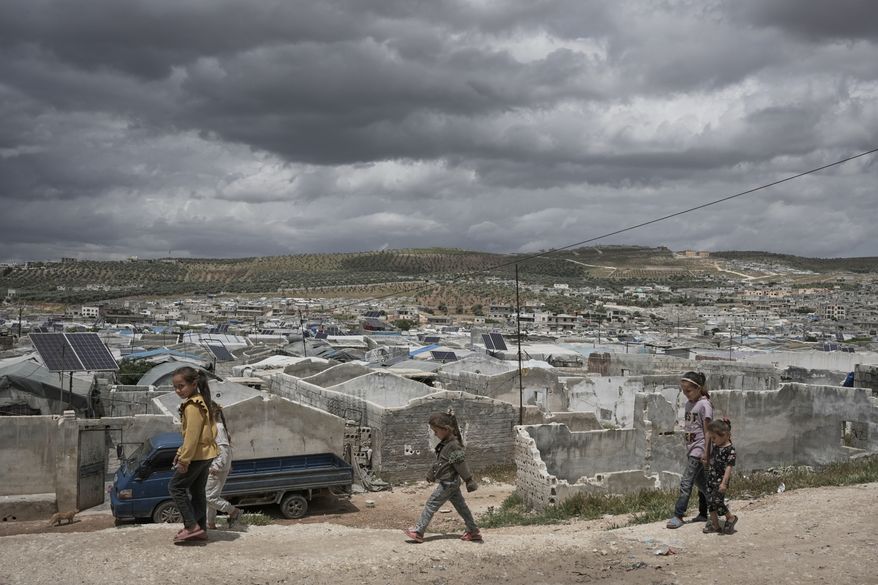 Syrian children walk along a dirt path at the edge of al-Karama camp, built from scratch with light-brick structures covered with fabric and housing internally displaced Syrians near the village of Atmeh, Idlib province, Syria, Tuesday, May 19, 2026. (AP Photo/Omar Albam)