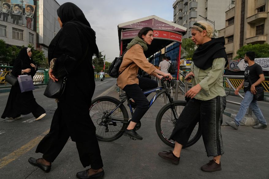 A woman rides a bicycle as others cross a street in downtown Tehran, Iran, Sunday, May 24, 2026. (AP Photo/Vahid Salemi)