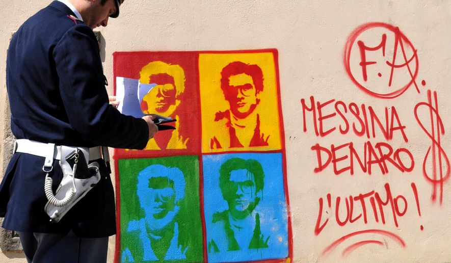 FILE - An Italian Police officer looks on at graffiti on the perimeter wall of Palermo's city's cathedral, portraying Matteo Messina Denaro, in Sicily, southern Italy, Thursday, April 24, 2008. (AP Photo/Alessandro Fucarini, File)