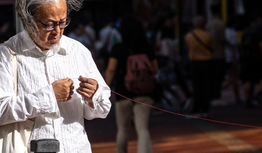 Artist Sanmu Chen displays a red thread as he performs on the street in the Causeway Bay area on the eve of the 37th anniversary of China's Tiananmen Square crackdown in Hong Kong, Wednesday, June 3, 2026. (AP Photo/Chan Long Hei)