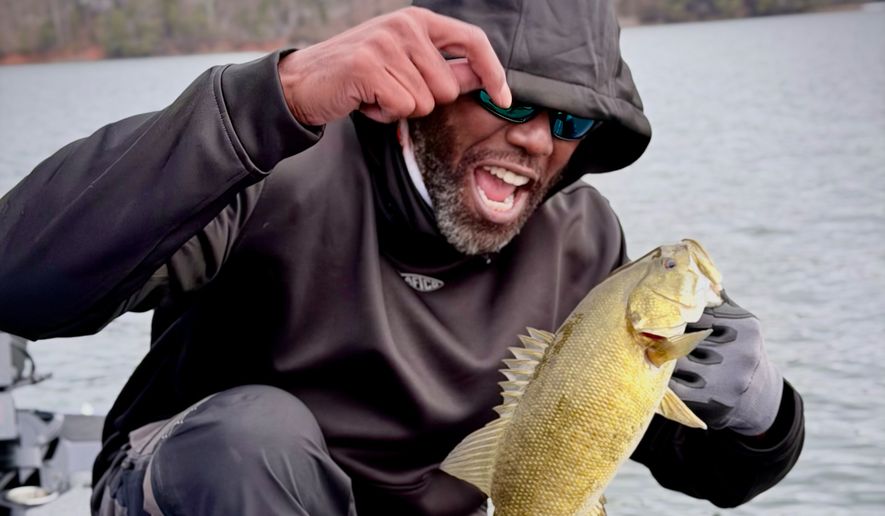 In this undated image provided by Andrew Grein, Hall of Fame wide receiver Randy Moss holds up a bass during the Chasing 10 with Randy Moss adventures series about Moss's chase for the legendary 10-pound largemouth bass. (Andrew Grein/Chasing 10 via AP)