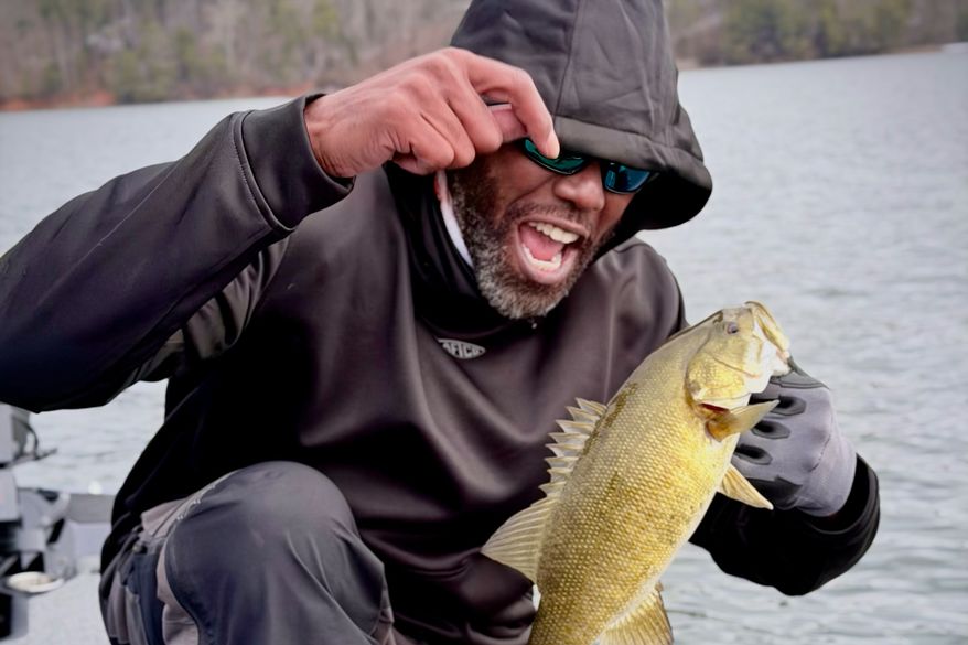 In this undated image provided by Andrew Grein, Hall of Fame wide receiver Randy Moss holds up a bass during the Chasing 10 with Randy Moss adventures series about Moss's chase for the legendary 10-pound largemouth bass. (Andrew Grein/Chasing 10 via AP)