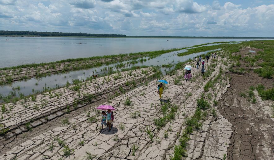 People walk through a part of the Amazon River that shows signs of drought in Santa Sofia, on the outskirts of Leticia, Colombia, Oct. 20, 2024. (AP Photo/Ivan Valencia, File)